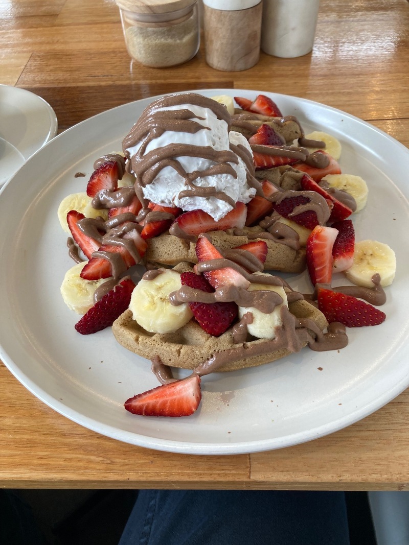 A plate of waffles with banana, strawberries, ice-cream, and chocolate sauce